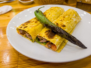Tortilla wrap with meat and vegetables on a white plate