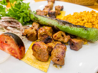 Meat kebab with vegetables on a white plate in a restaurant