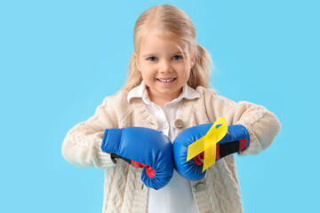 Cute little girl in boxing gloves with yellow ribbon on blue background. Childhood cancer awareness concept