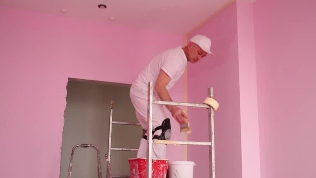 Builder with brush in hand painted walls in pink room 
