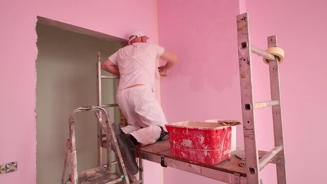 Plasterer standing on scaffolding in pink room and work
