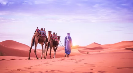 Gordijnen Camel rider with camels travelling over dunes in the desert © Eliya