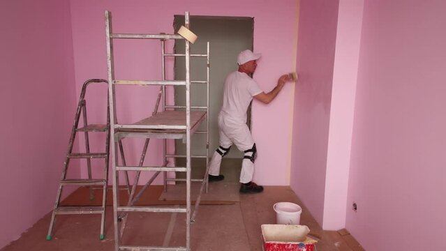 Plasterer in white clothes and kneepads works in new room