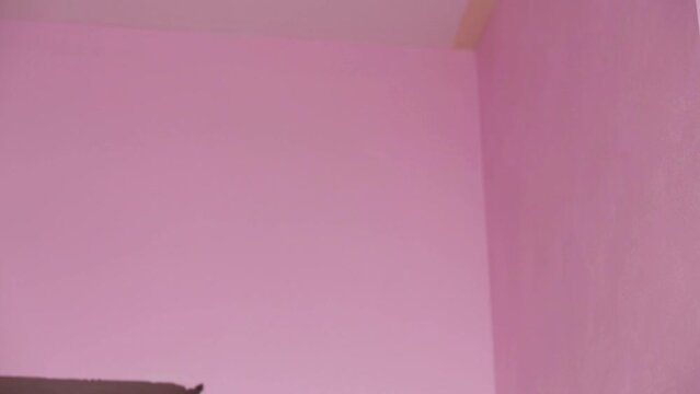 Painter in white clothes removes masking tape in pink room