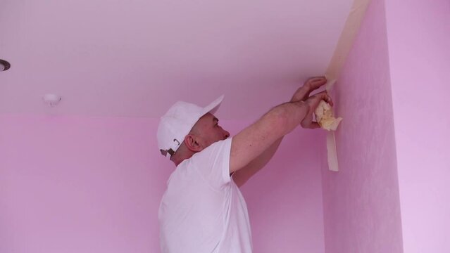 Colourer in white clothes removes masking tape in pink room