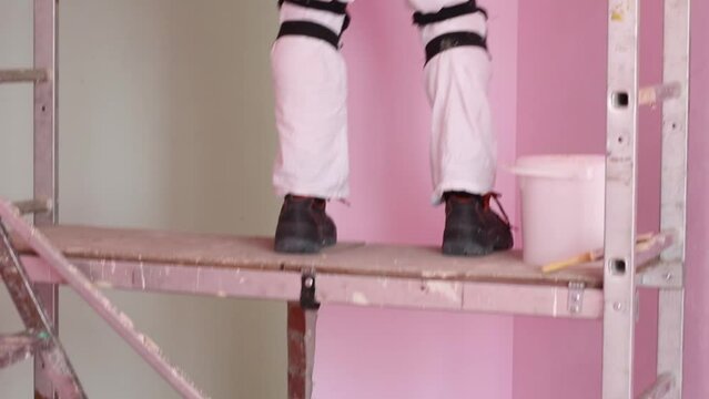 Finisher with brush on scaffolding paints wall in new pink room