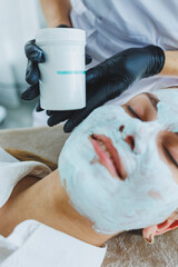 The office of a beautician applying a mask to a woman's face in a spa salon, view above. Aesthetic procedure. Care mask for facial skin.