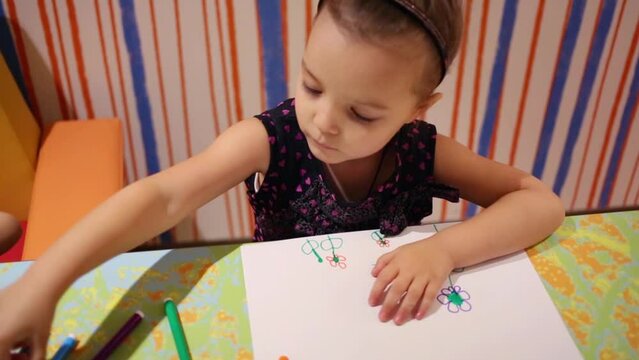 Little pretty girl draws flowers with colored markers at table