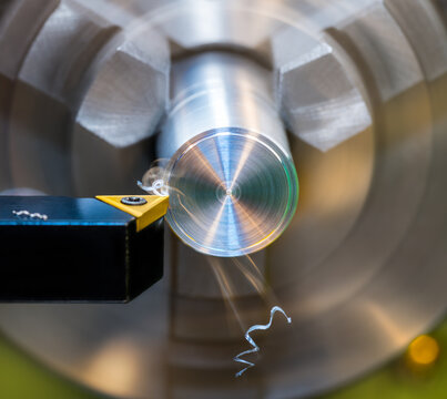 Closeup a black tool bit with sharp cutting edge on yellow carbide insert at turning. Lathe machine at working dural workpiece clamped in chuck jaws with beautiful blurry motion of flying metal swarf.