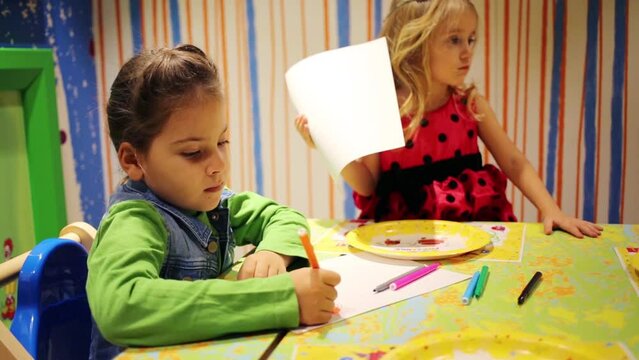 Little girl draws and other girl holds paper in room in McDonalds
