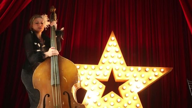 woman plays old damaged contrabass and dances on stage.