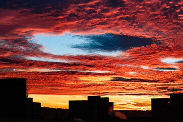 Beautiful sunset with fallstreak hole in red fiery sky and a buildings silhouette. Majestic orange...