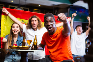 Happy excited African American watching football game in sports bar, making winner gesture after...