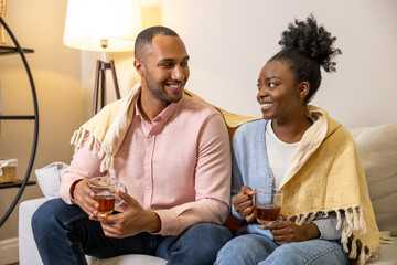 Man and woman drinking tea while watching tv sitting on couch in home interior