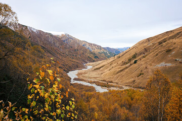 Winding River Through Autumnal Mountain Valley. A sinuous river carves through a valley blanketed in the vibrant colors of fall, framed by the rolling hills and distant peaks