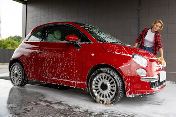 Blonde young woman washing a car and feeling positive