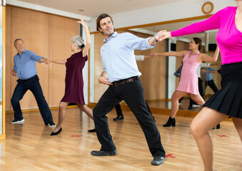 Positive adult man enjoying active dances with female partner in modern dance studio, practicing playful jitterbug moves