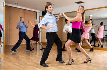 Spirited middle-aged pair training Latino dance during workout session. Pairs training ballroom dance in hall