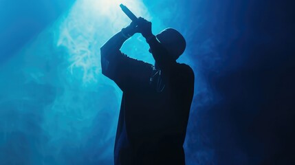 Silhouette of rap singer performing on stage. Bright blue background with hip hop artist performing on concert in night club