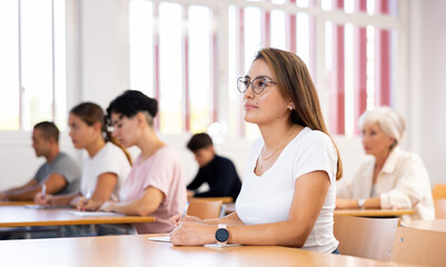 Latin woman attending lecture in college, listening lecture with group of students.