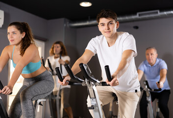 Sportive people in activewear warming up on training using exercise bike in gym