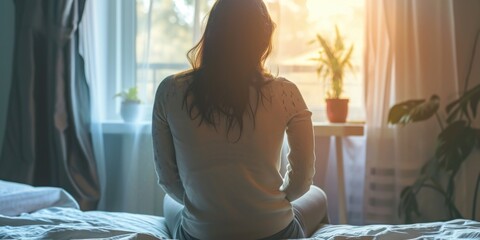 A woman sitting on a bed, gazing out of a window. Suitable for various lifestyle and introspection themes