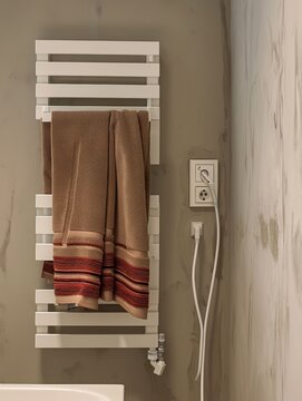 Generative AI image of a beige-colored wall with a white, wall-mounted towel radiator on which hangs a brown towel with a stripe pattern and a hint of red.