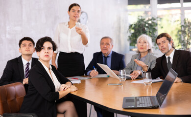 Focused interested young Hispanic businesswoman sitting at table in office, listening attentively to presentation of partners during business meeting