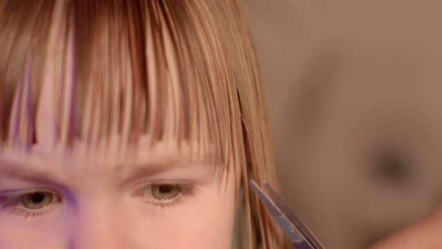 Routine grooming session for babies. Close-up scene, the camera focuses on the expressive eyes of a little girl as she maintains eye contact while having her bangs trimmed with scissors. 