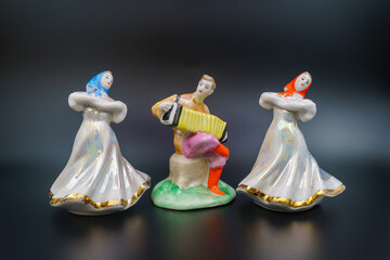 Ensemble, porcelain figurines, ceramic girls flanking accordion player, dresses traditional attire, folk hand-painted