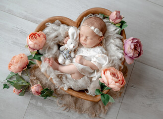 Newborn Baby Girl Sleeps In Heart-Shaped Wooden Bowl Among Flowers During Studio Photoshoot