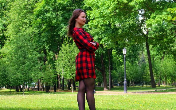 A young beautiful girl in a red plaid shirt and skirt in a park.