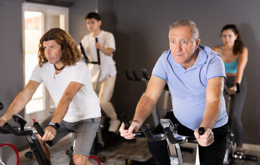 Fototapeta na wymiar Focused aged man leading healthy active lifestyle doing cardio workout on exercise bike in gym
