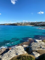 Bay and coastline of an island. View of the city in the distance. View of turquoise waves breaking on the shore. Rocky coast of the ocean. Landscape and shore. Australia, Sydney.