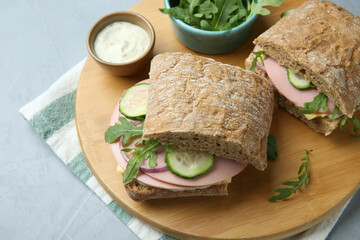 Tasty sandwiches with boiled sausage, cucumber, arugula and sauce on grey table, closeup