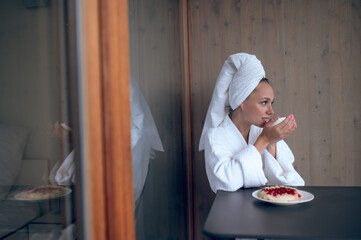 Young woman in white robe having breakfast and feeling good