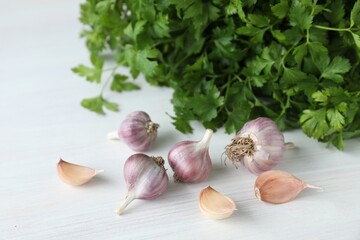 Fresh raw garlic and parsley on white wooden table, closeup