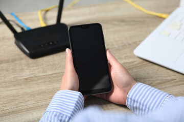 Woman with smartphone connecting to internet via Wi-Fi router at wooden table indoors, closeup