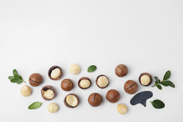 Tasty Macadamia nuts and green leaves on white background, flat lay. Space for text