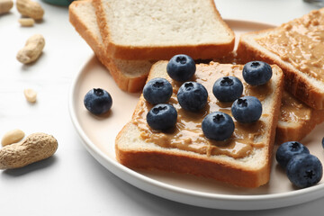 Delicious toasts with peanut butter and blueberries on white table, closeup