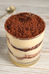 Delicious tiramisu in glass on light wooden table, closeup