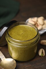 Tasty pistachio cream in jar and nuts on wooden table, closeup