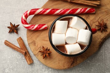 Tasty hot chocolate with marshmallows, candy cane and spices on light grey table, flat lay