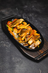Fried fish with vegetables in a frying pan on a dark background.