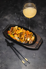Fried fish with vegetables in a frying pan on a dark background.