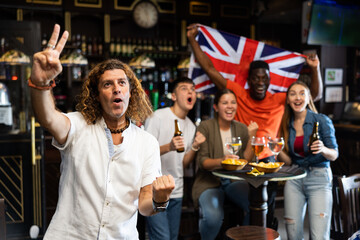 Happy multiracial friends holding the flag of Great Britain, supporting national football team in...