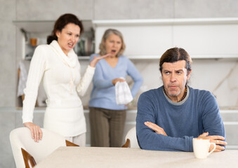 Wife and elderly mother actively prove something to man in kitchen