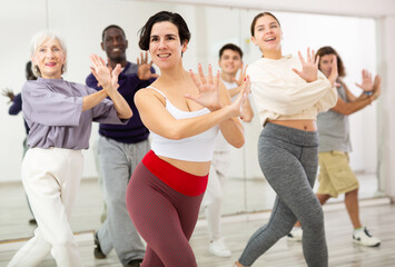 Smiling young woman rehearsing modern dance with group in dance school