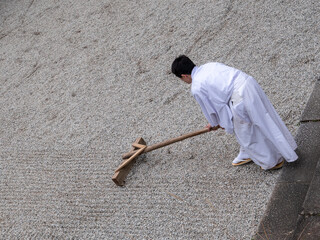 A monk rakes a gravel garden at Kasuga Taisha Shrine in Nara, Japan with an old wooden rake.