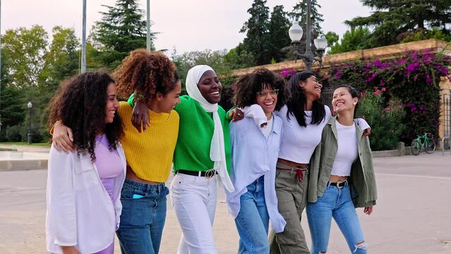 Multi ethnic group of joyful beautiful women having fun together outdoors. Diverse female friends hugging each other while walking at city street. Friendship and female community concept. Slow motion